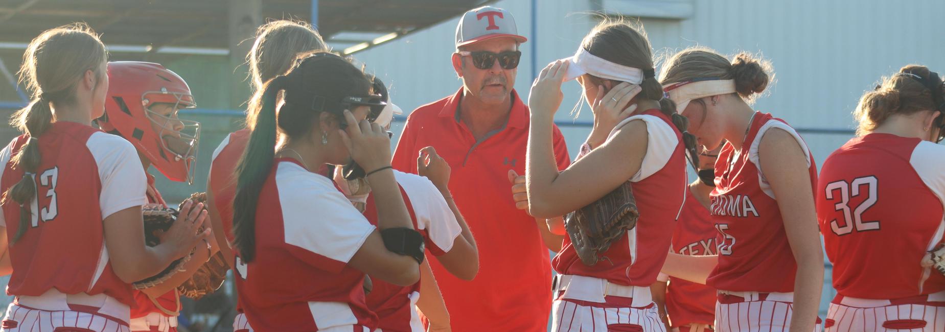 A softball team huddles together during a game with their coach giving instructions.