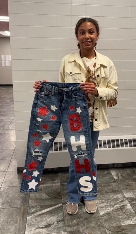 Girl holding decorated jeans featuring stars and letters in BHHS colors.