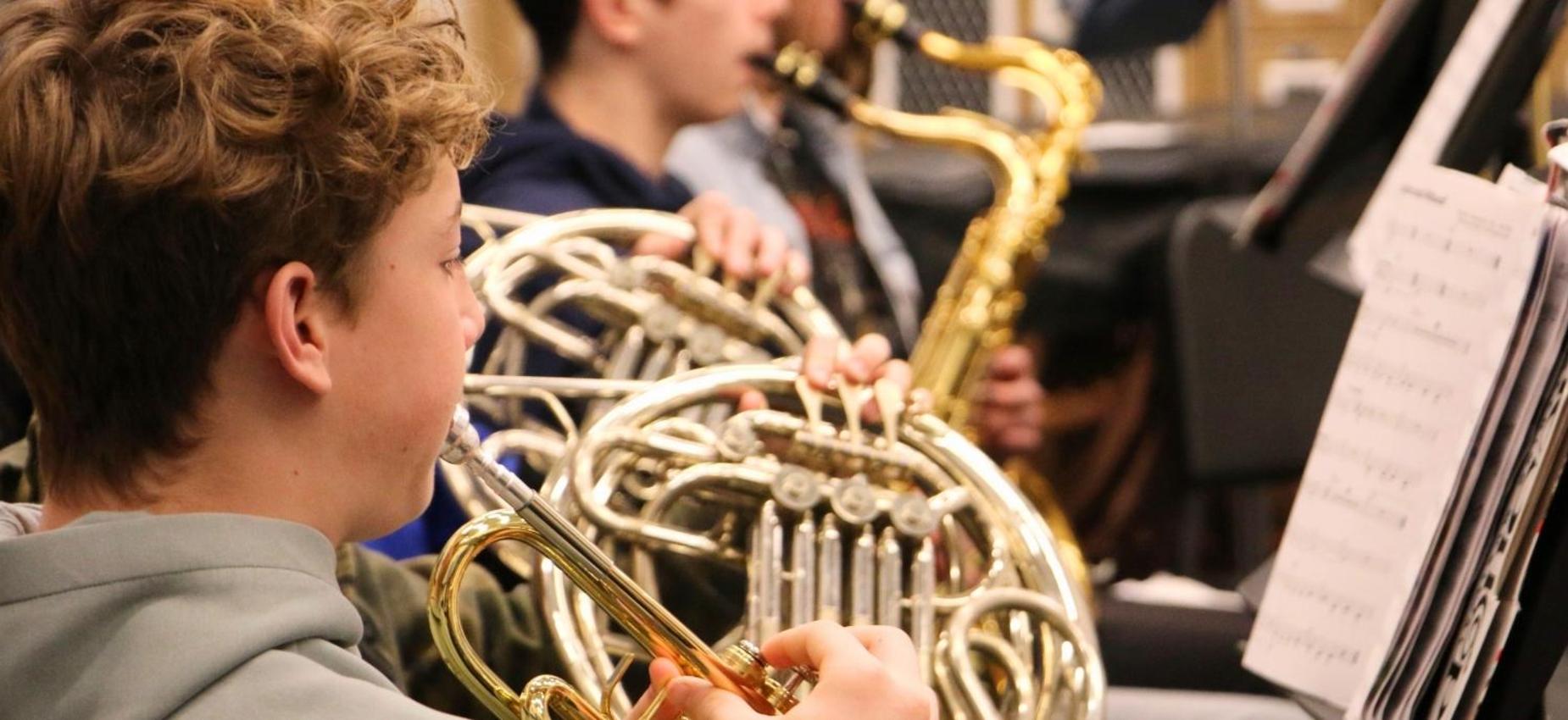 A young musician playing a French horn in a band setting.
