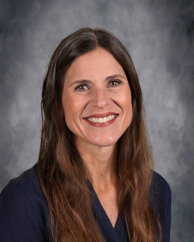 Smiling woman with long brown hair, wearing a green top against a gray backdrop.
