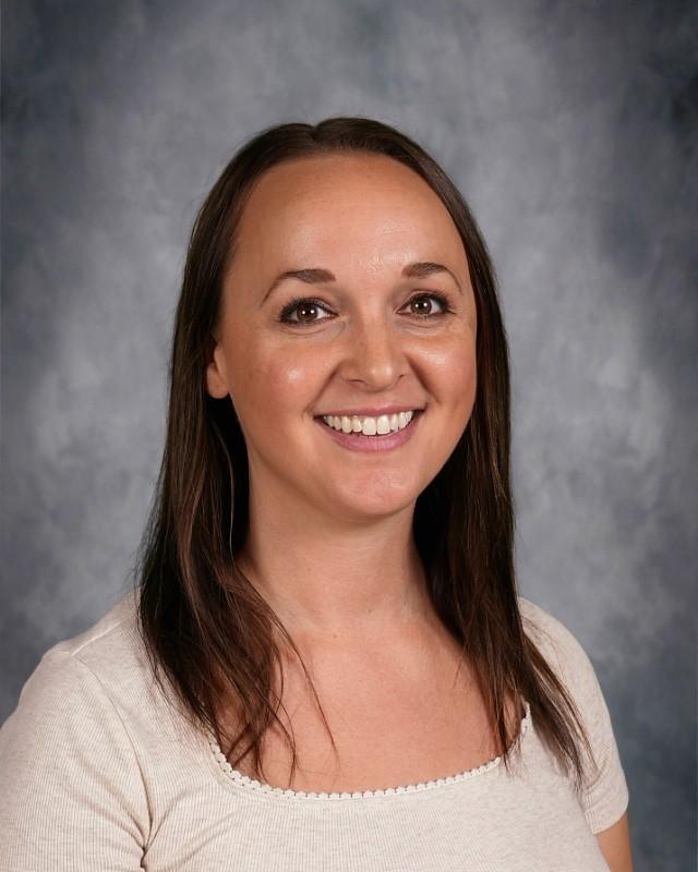 Smiling woman with long black hair in a white sweater against a gray background.