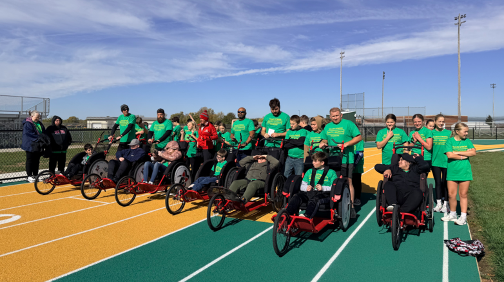 Group of individuals in green shirts on a running track with wheelchairs.