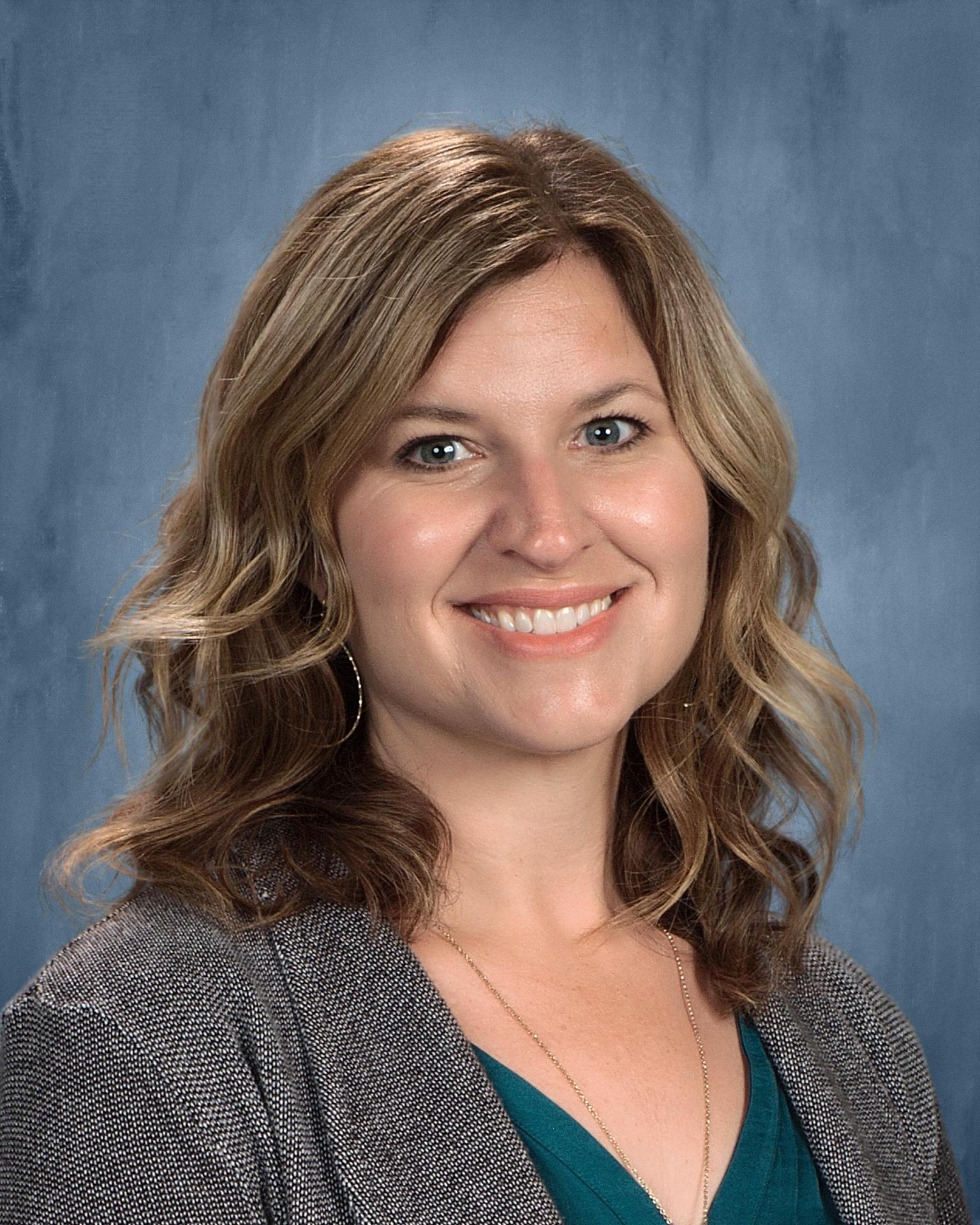 photo of teacher with blond/brown wavy hair, teal shirt, and blazer
