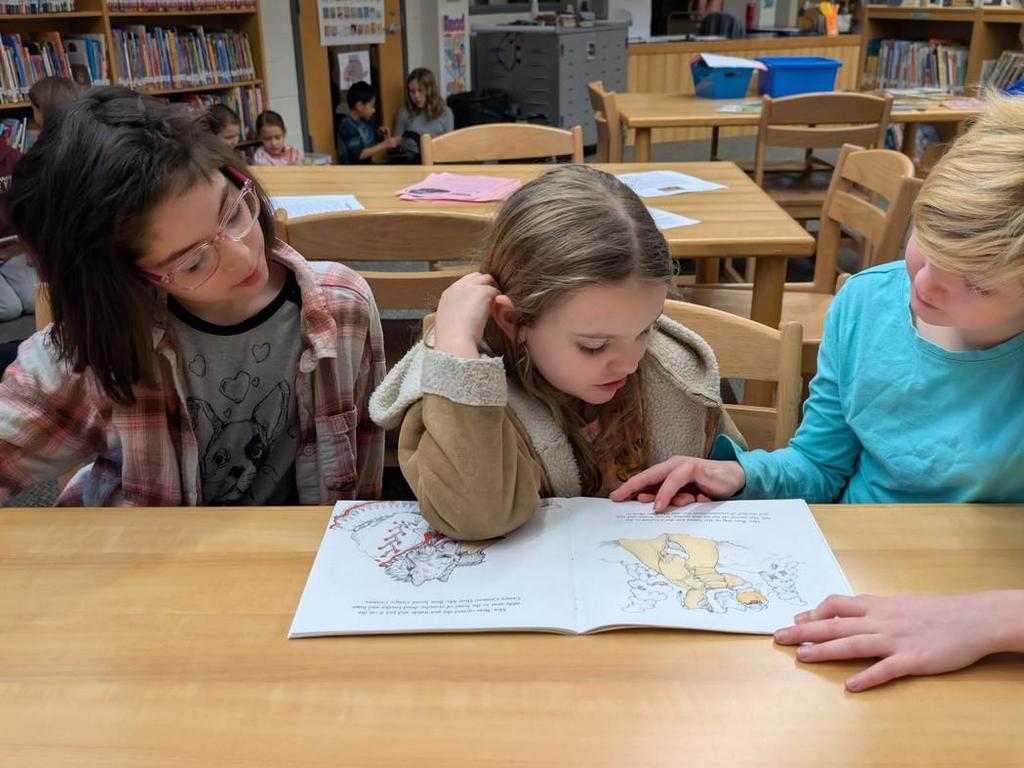 Three students reading to one another in the library.