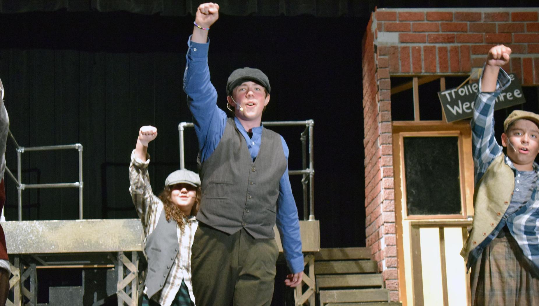 Two actors performing on stage with raised fists in a theatrical setting.