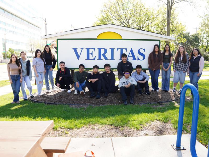 A large group of Veritas students smiling in front of the school's sign