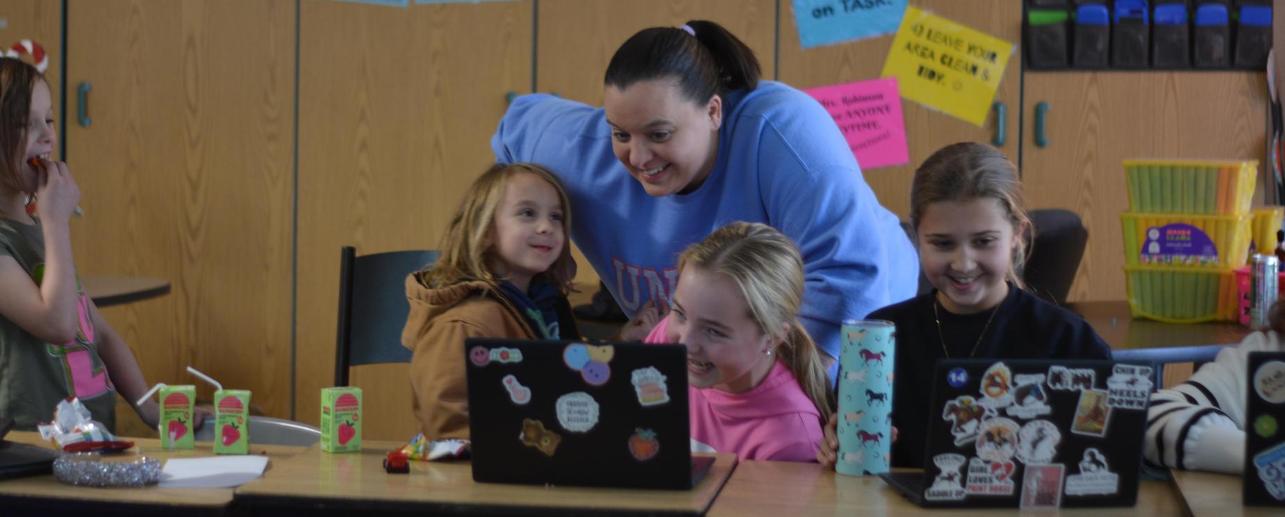 Teacher with students smiling at a computer