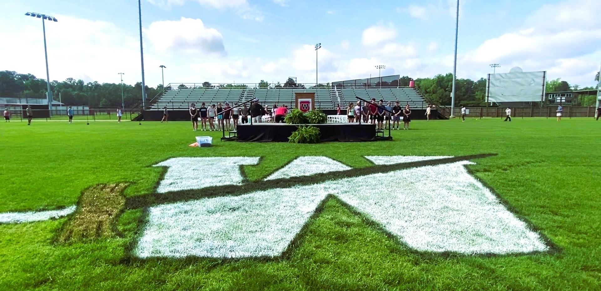 Graduation ceremony setup on a green field with a large 'W' logo.