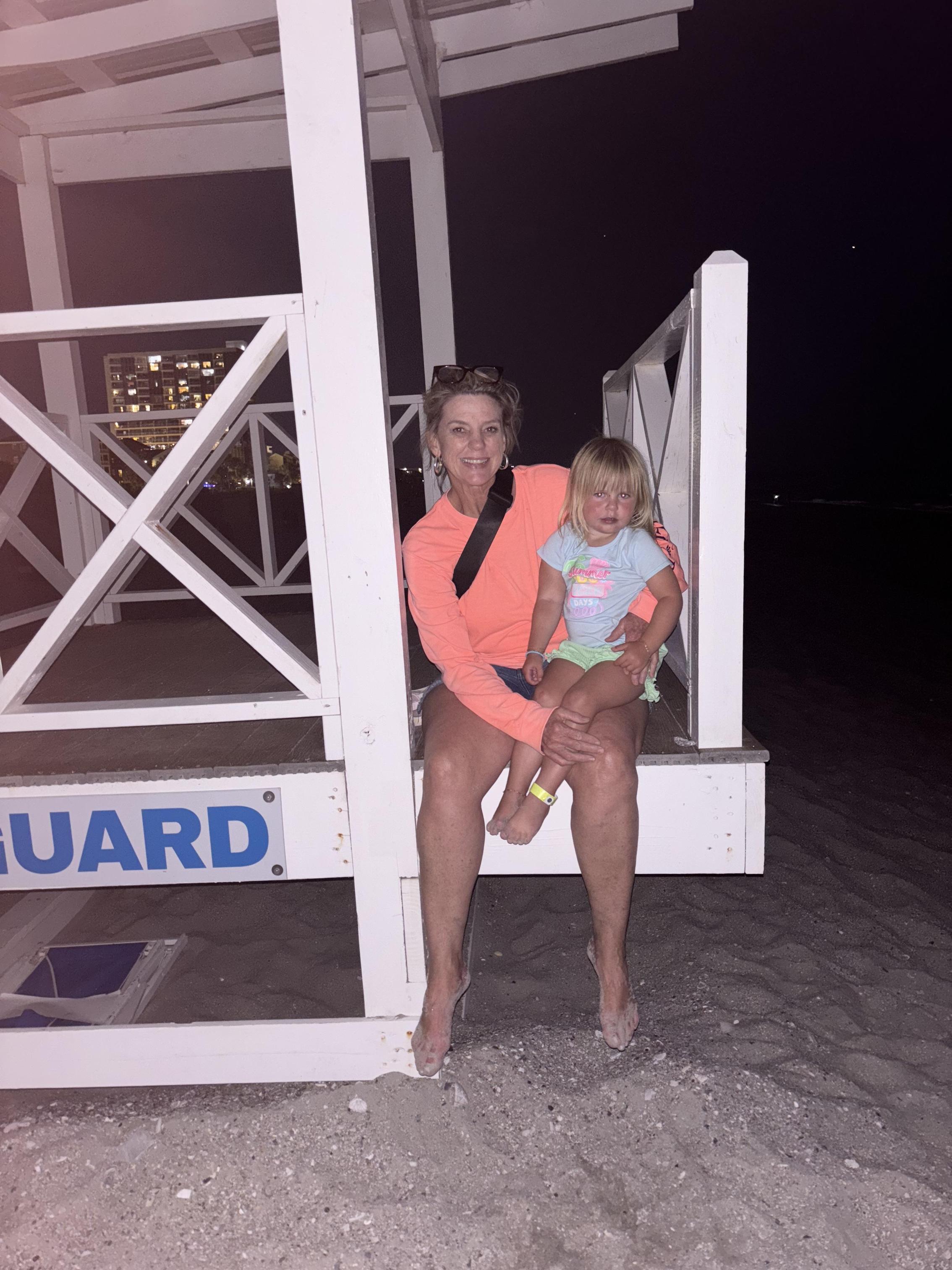 A woman and a child sitting on a lifeguard stand at night.