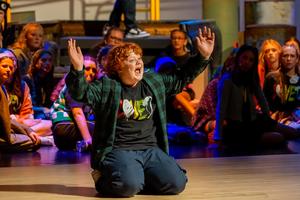 Single cast of Godspell on his knees with arms wide.
