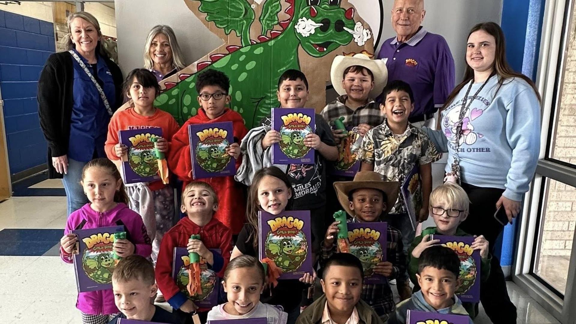 Group of children holding books, posing with adults in front of a colorful backdrop.