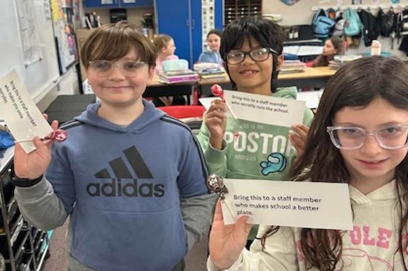 Three students hold up notes that they selected to give staff