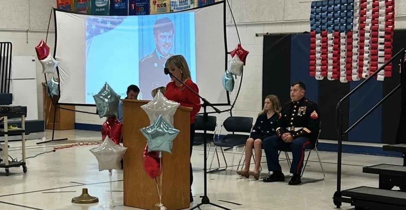 Speaker at an event addressing an audience with balloons and guests seated nearby.