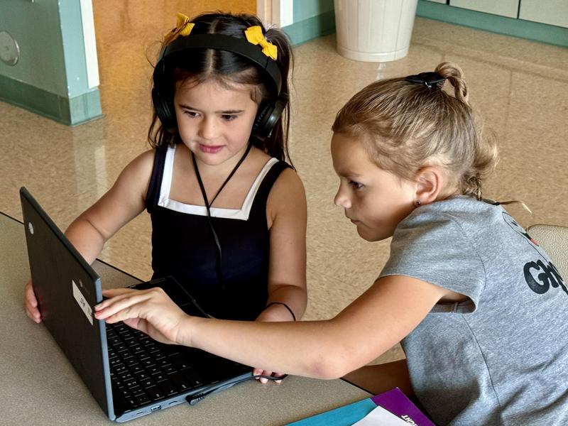Two elementary school students look carefully at a laptop screen