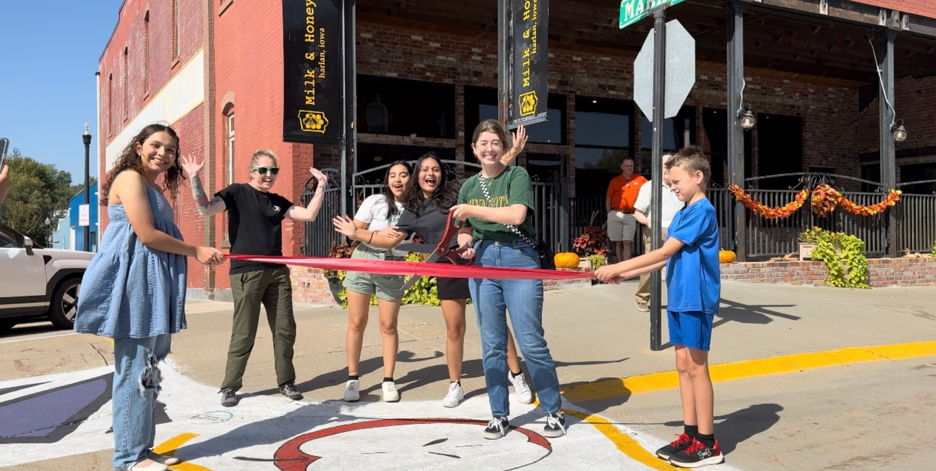 A group of people celebrating a ribbon-cutting event outside a brick building.