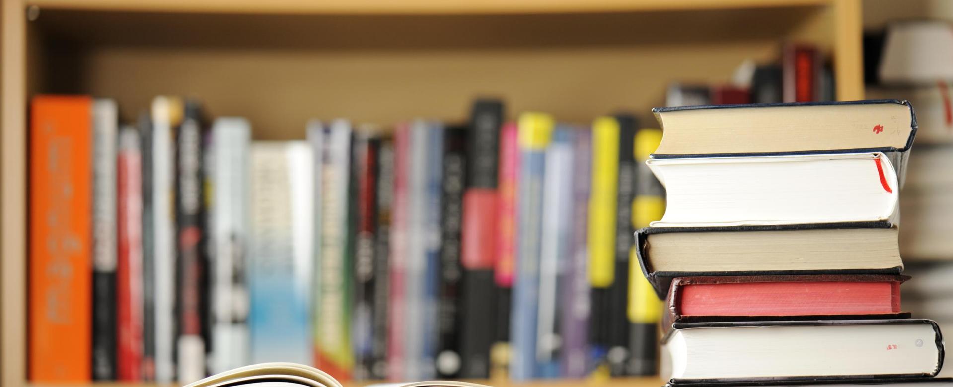 An open book in front of a stack of closed books on a wooden surface.