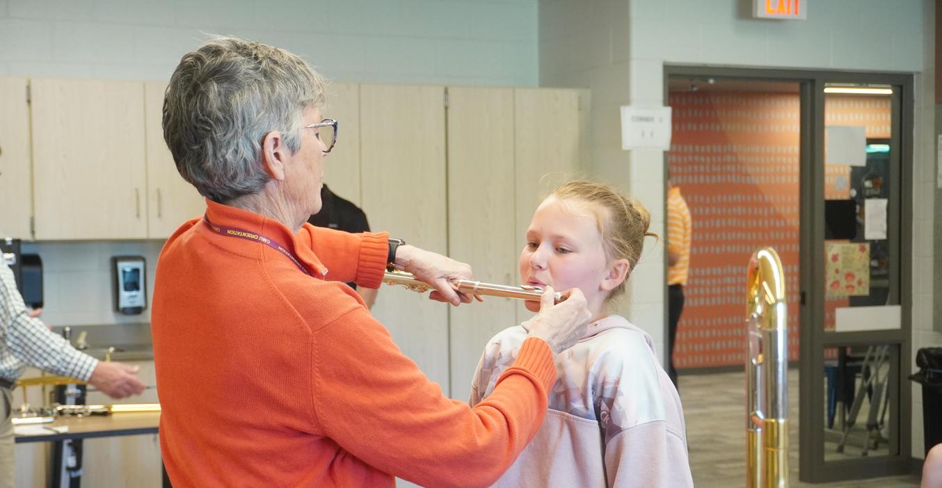 An adult teaches a child how to play a flute in a classroom.