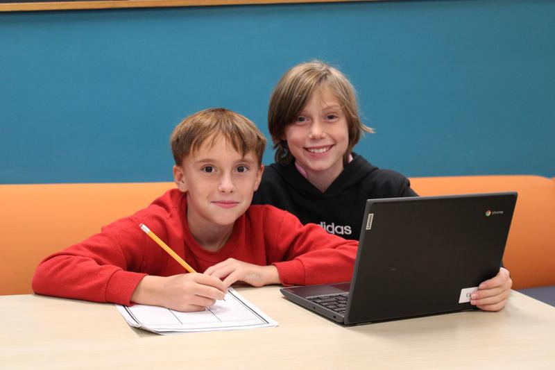 Two boys at a computer, smiling at the camera