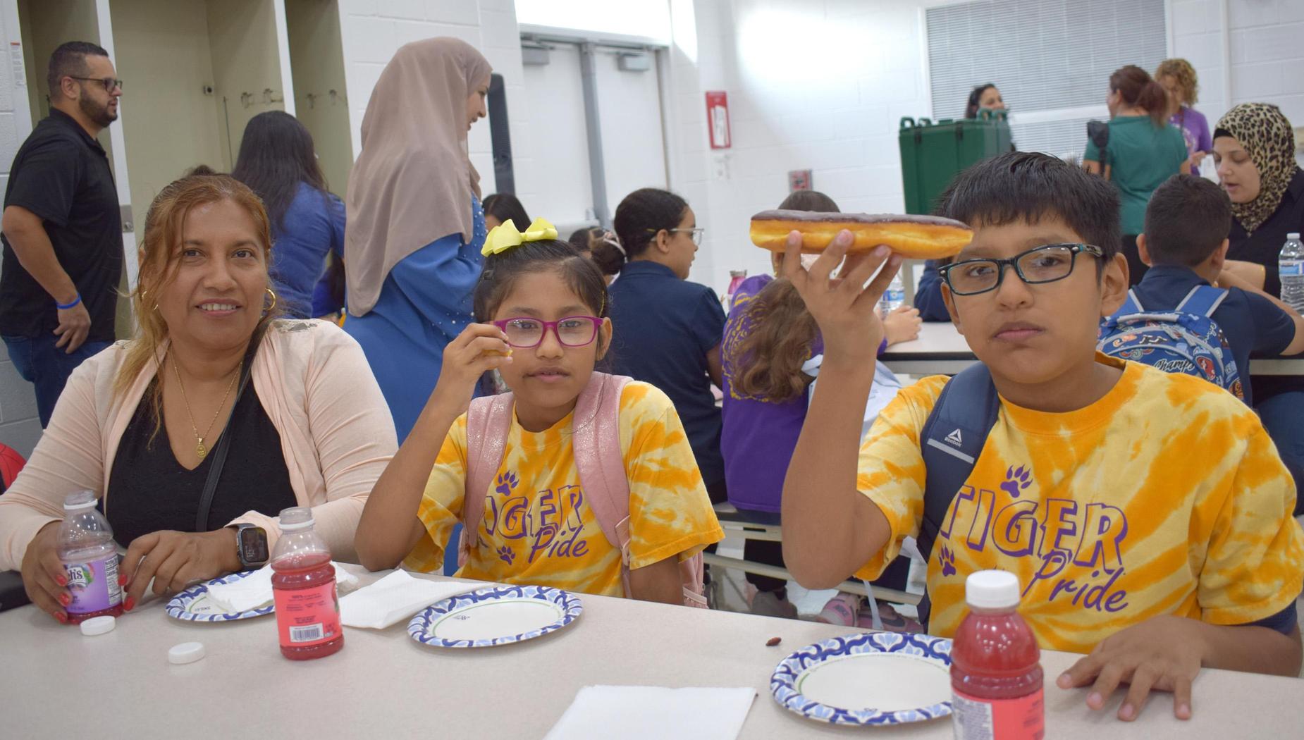 A mother and her children enjoying donuts at a school event.