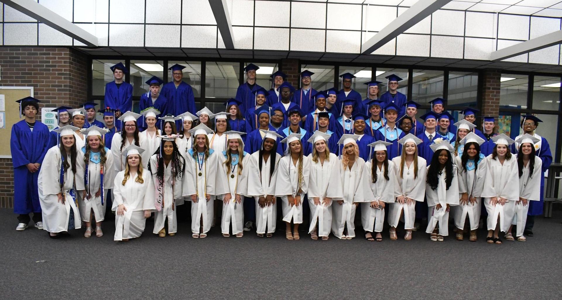 Group of graduates in blue and white gowns, smiling together indoors.