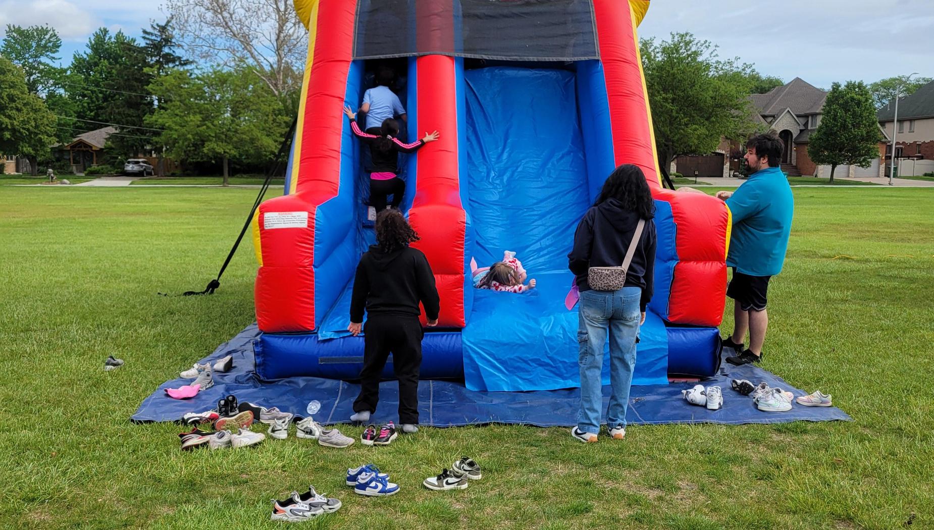 Participants climbing a red and blue inflatable slide at an outdoor event with shoes around.