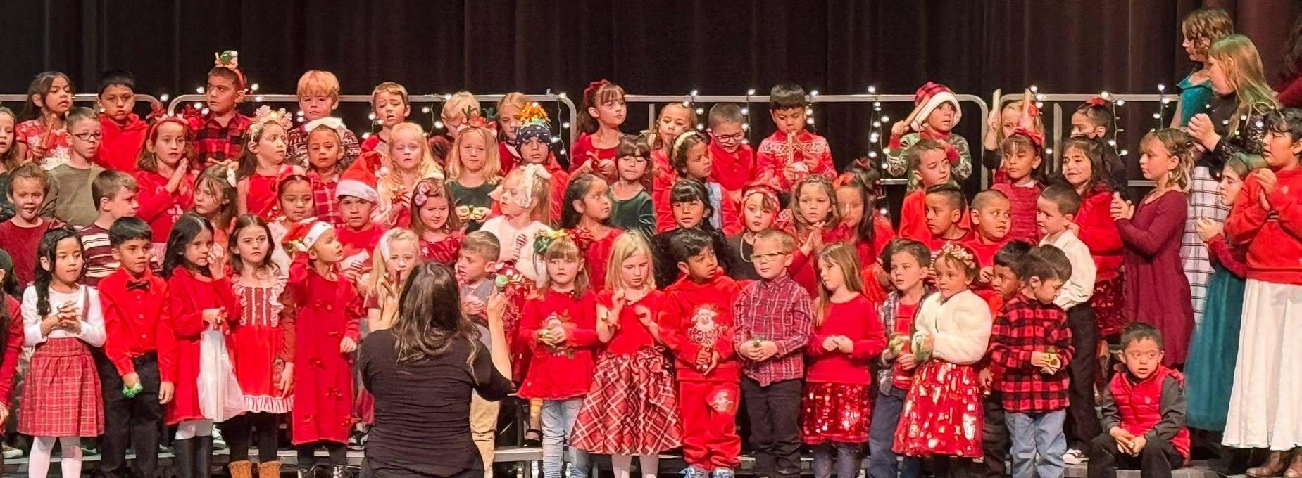 Children in festive attire perform on stage during a holiday event.