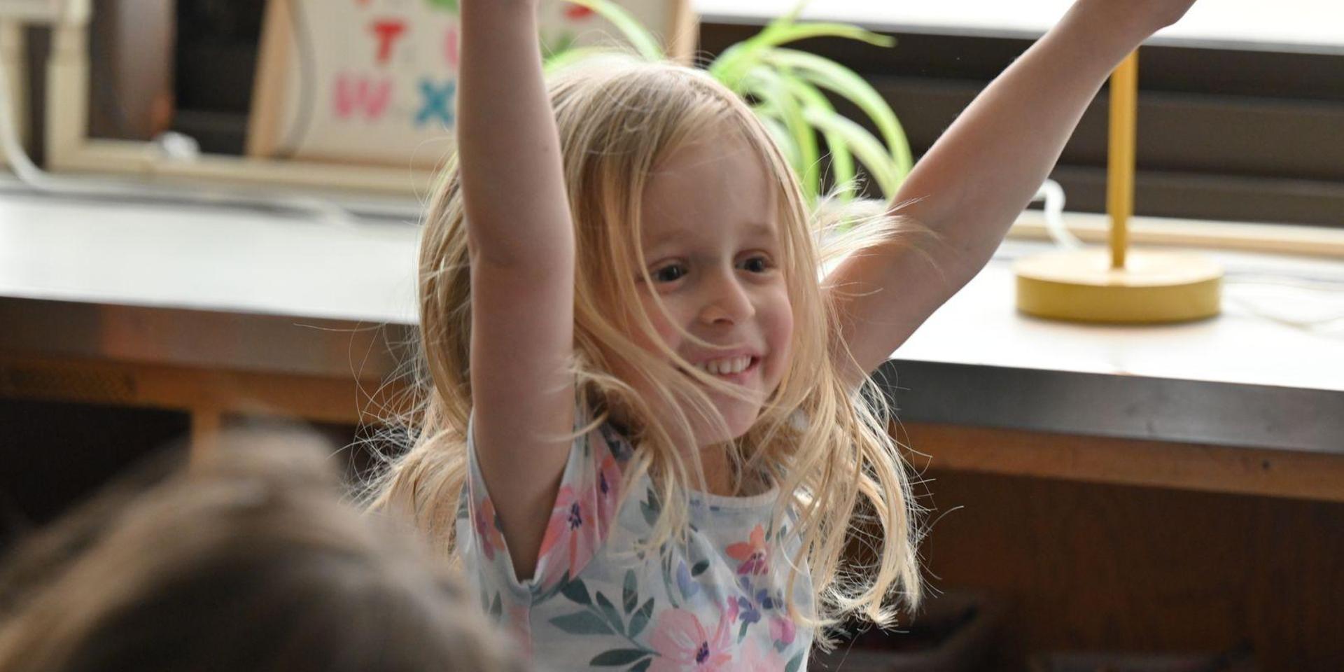 A young girl celebrating with raised arms, smiling broadly.
