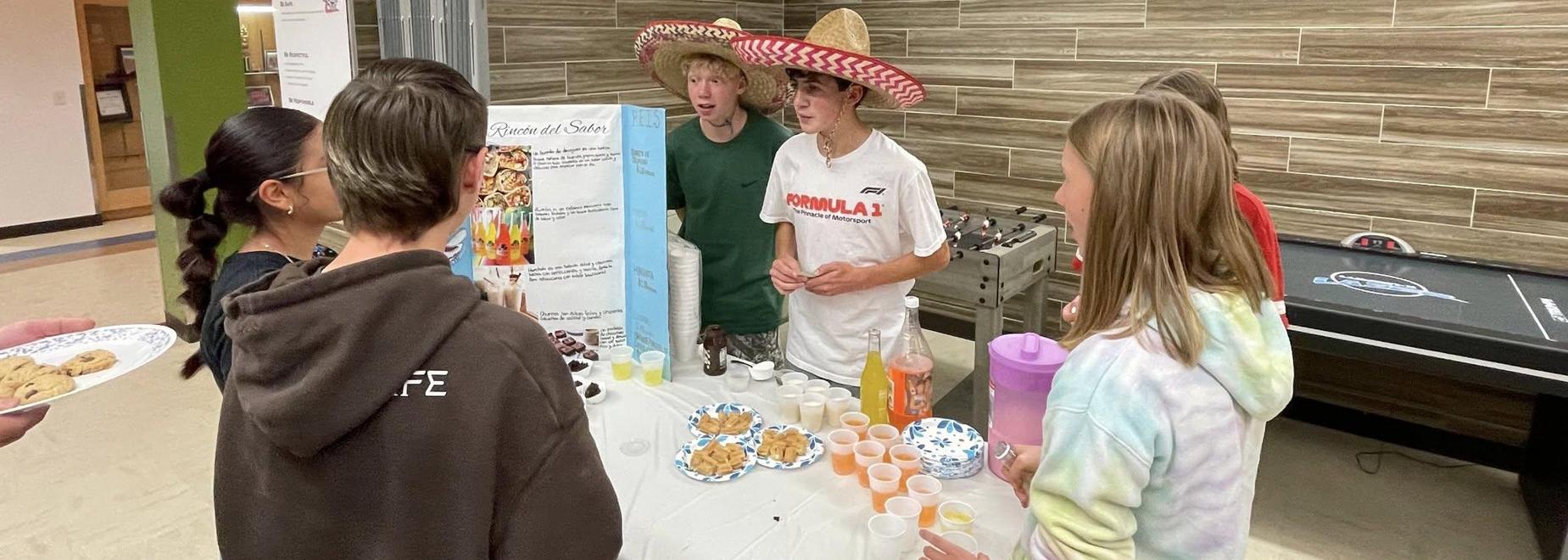 Two young boys wearing sombreros serve desserts to a group of curious peers.