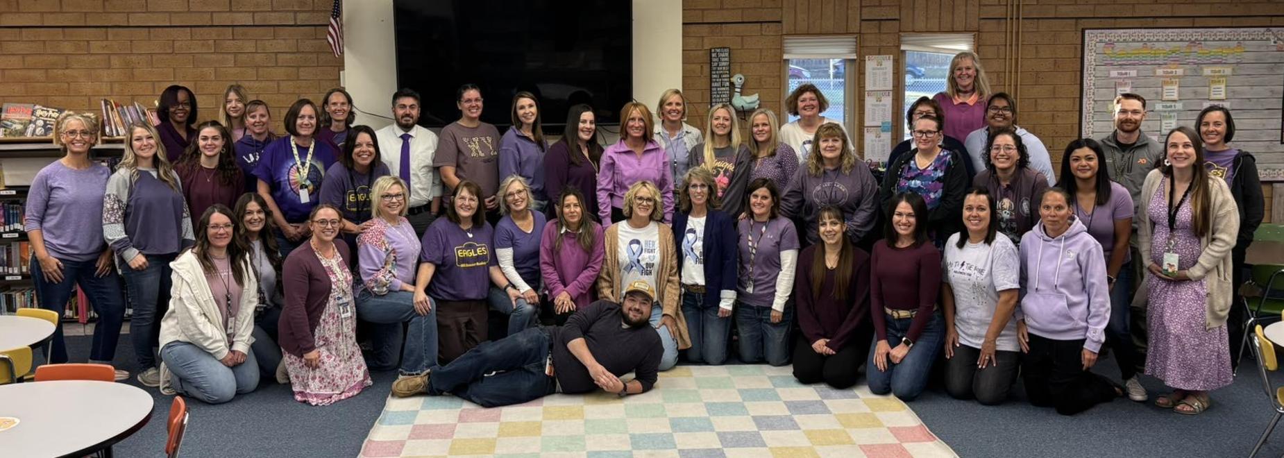A large group of diverse individuals gathered in a library, mostly wearing purple attire.