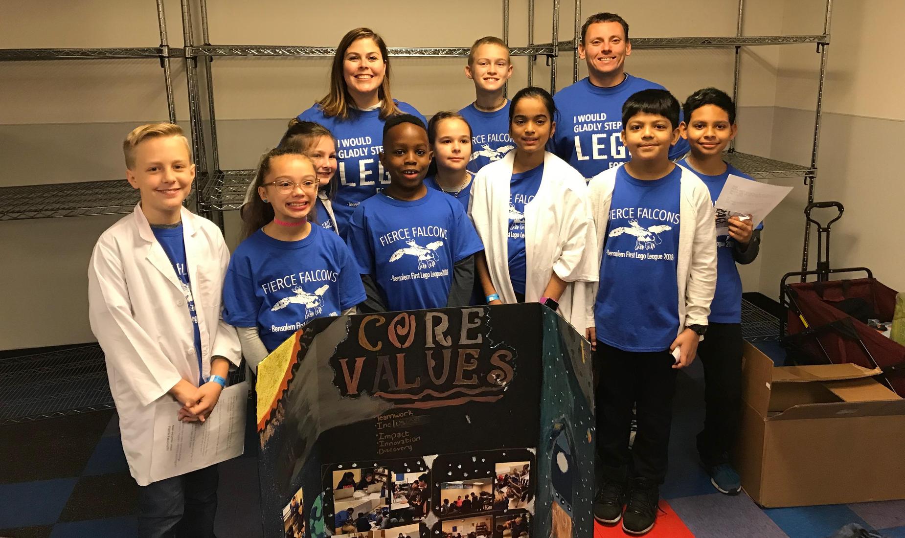 9 boys and girls and their teachers dressed in blue Fierce Falcons shirts ready for their First Lego League Competition