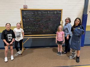 student leaders and art teacher in front of sign welcoming families