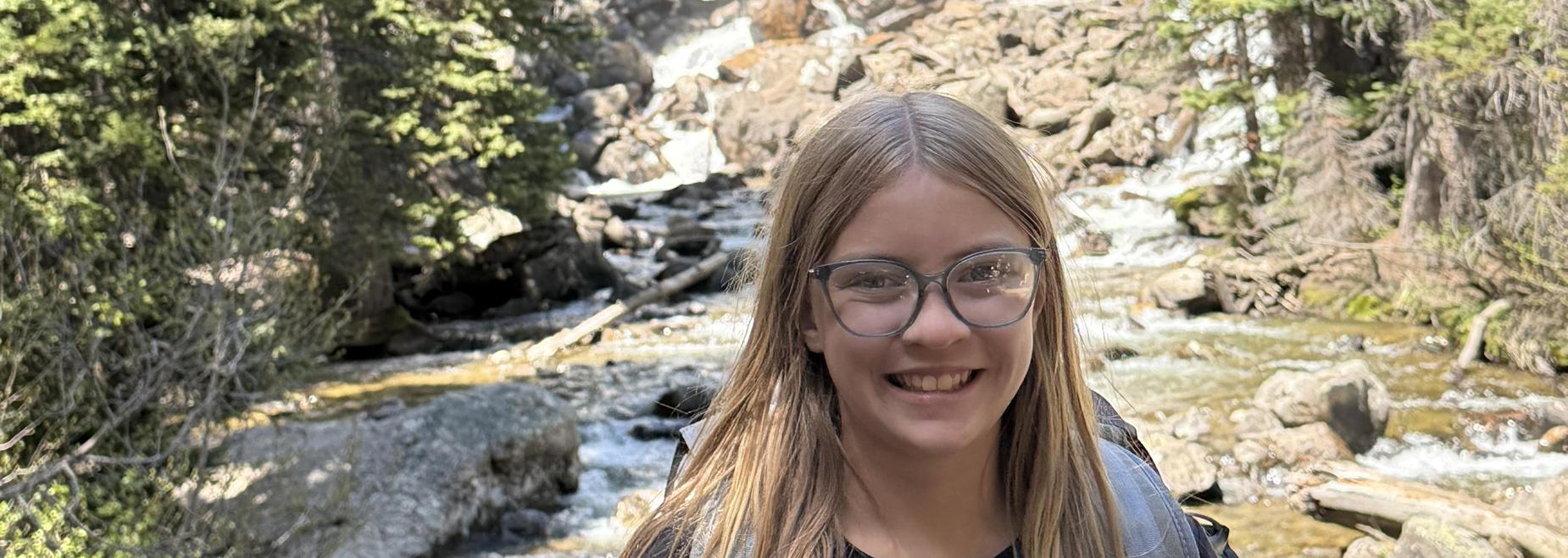 Young girl smiling in front of a waterfall surrounded by trees.