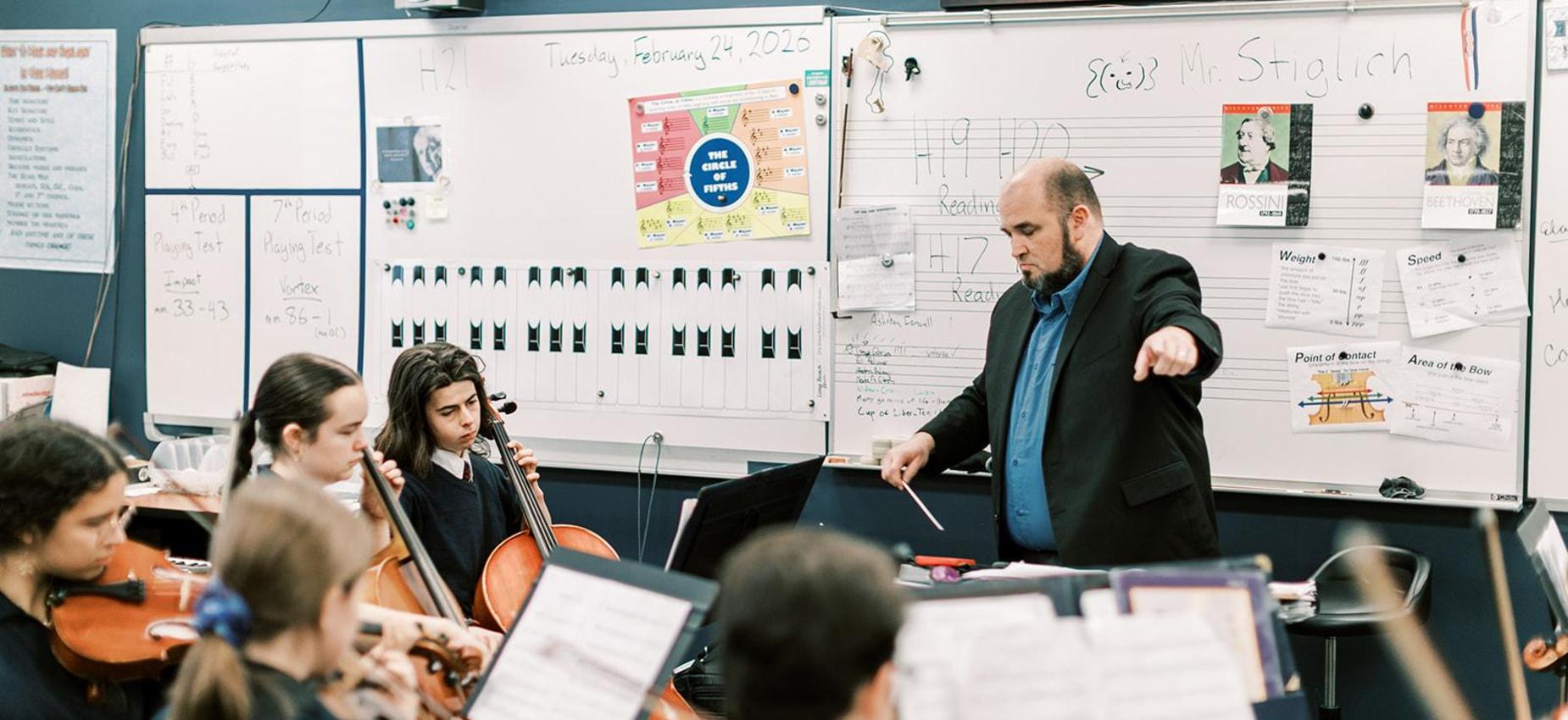 Orchestra director conducts a high school string rehearsal