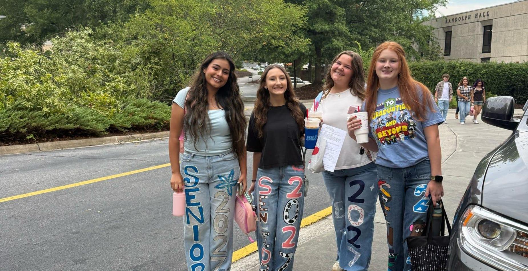 Four students pose together in decorated jeans on a campus pathway.