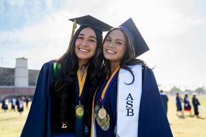 Two female graduates from California High School smile at the camera prior to their graduation ceremony.