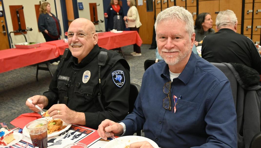 Two men sitting at a table enjoying a meal, smiling at the camera.