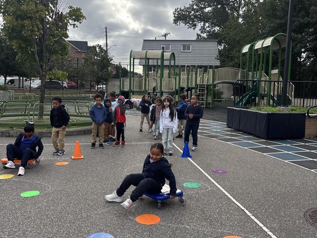 Children playing on a playground with cones and equipment in the background.