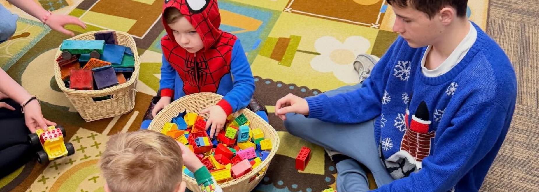 Children playing with colorful building blocks on a patterned rug.