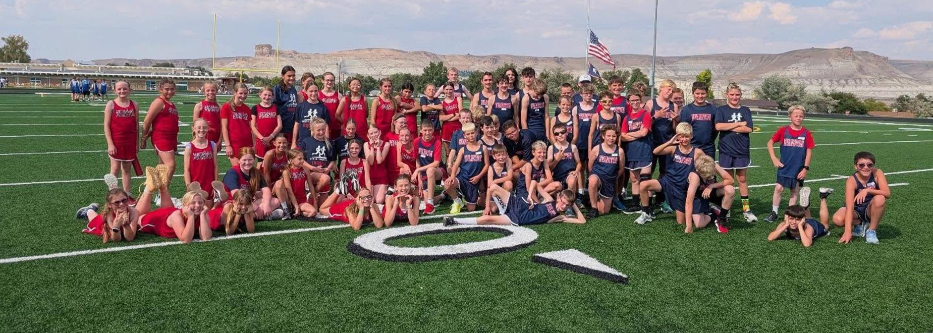 Large group of young runners posing together on a football field with a scenic background.