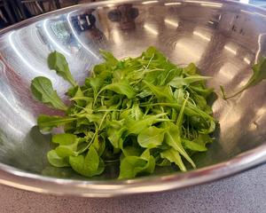 Freshly harvested green lettuce leaves sit inside a large metal bowl on a table.