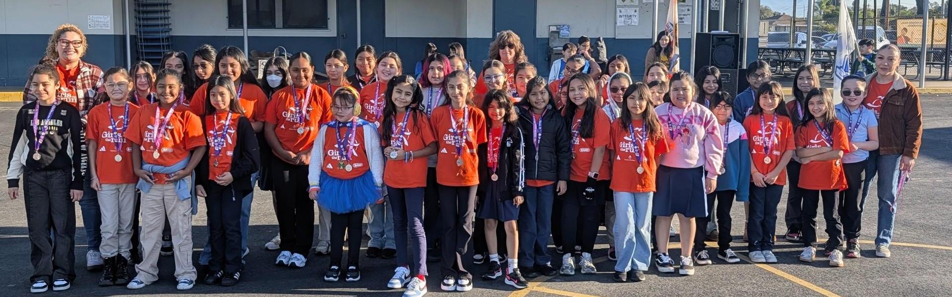 A large group of children in orange shirts standing outside a building.