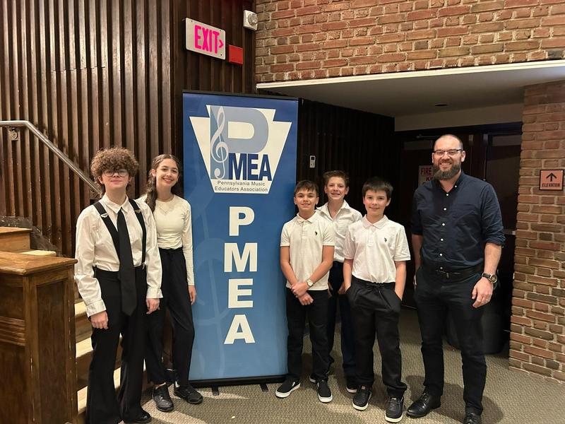 5 students and teacher standing beside pmea sign