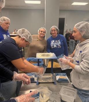A group of volunteers in hairnets and gloves preparing food in a communal kitchen.