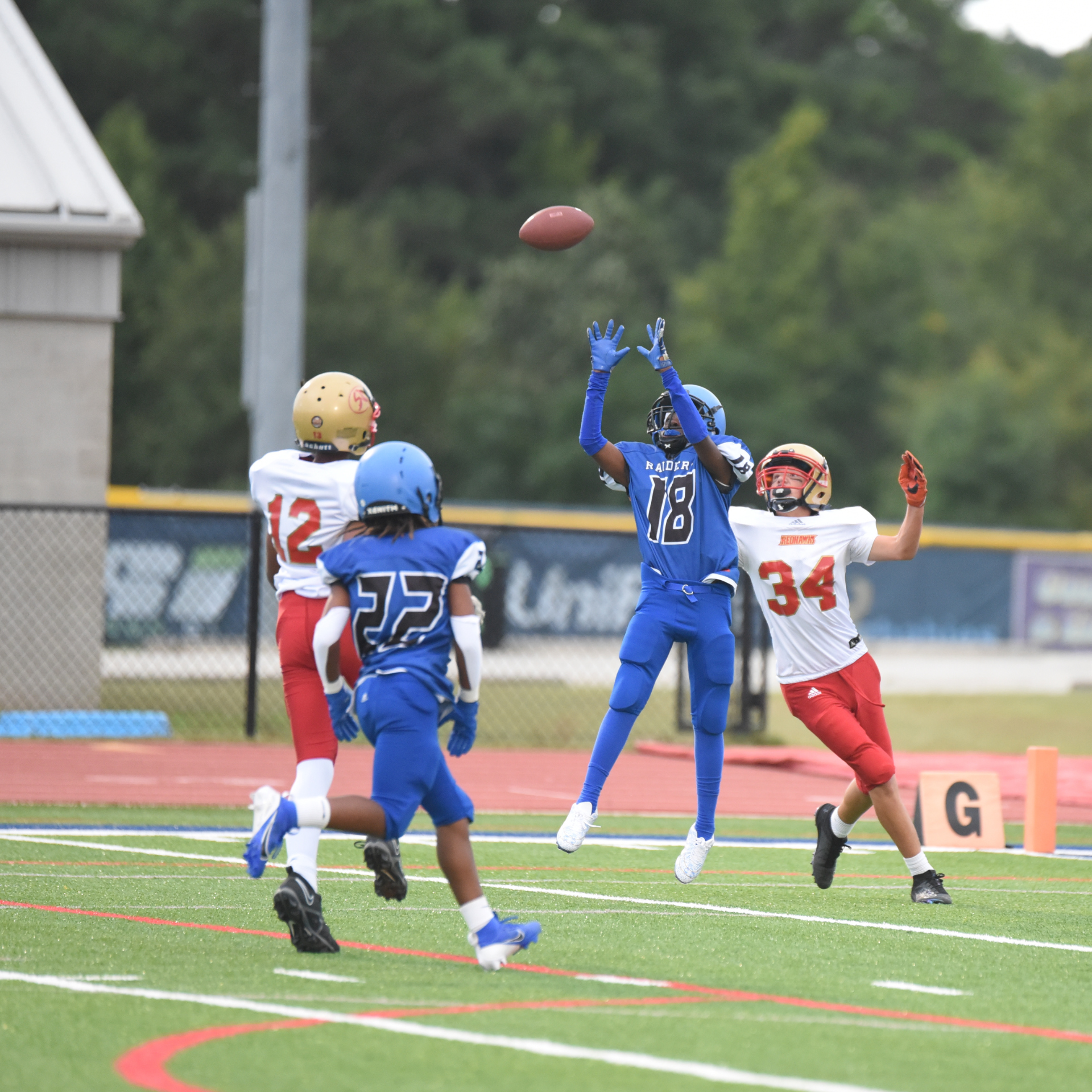 Player in blue jumps to catch a football amidst approaching defenders on the field.