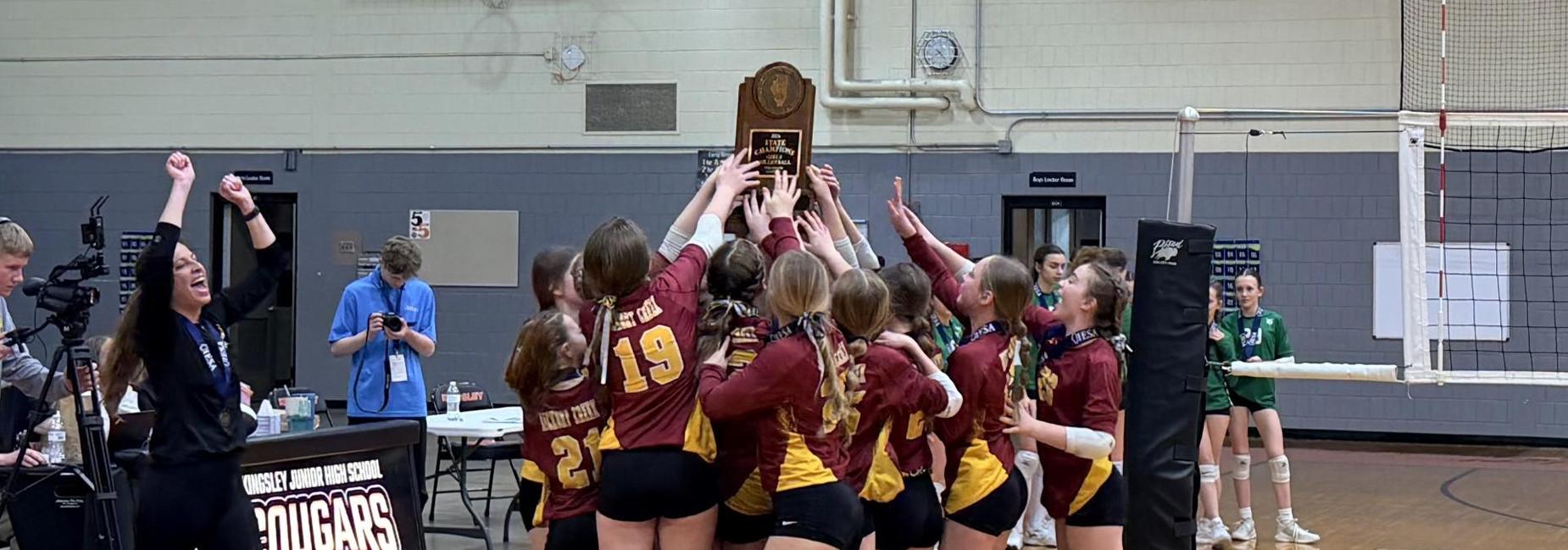 A volleyball team celebrating a victory, holding a trophy and cheering.
