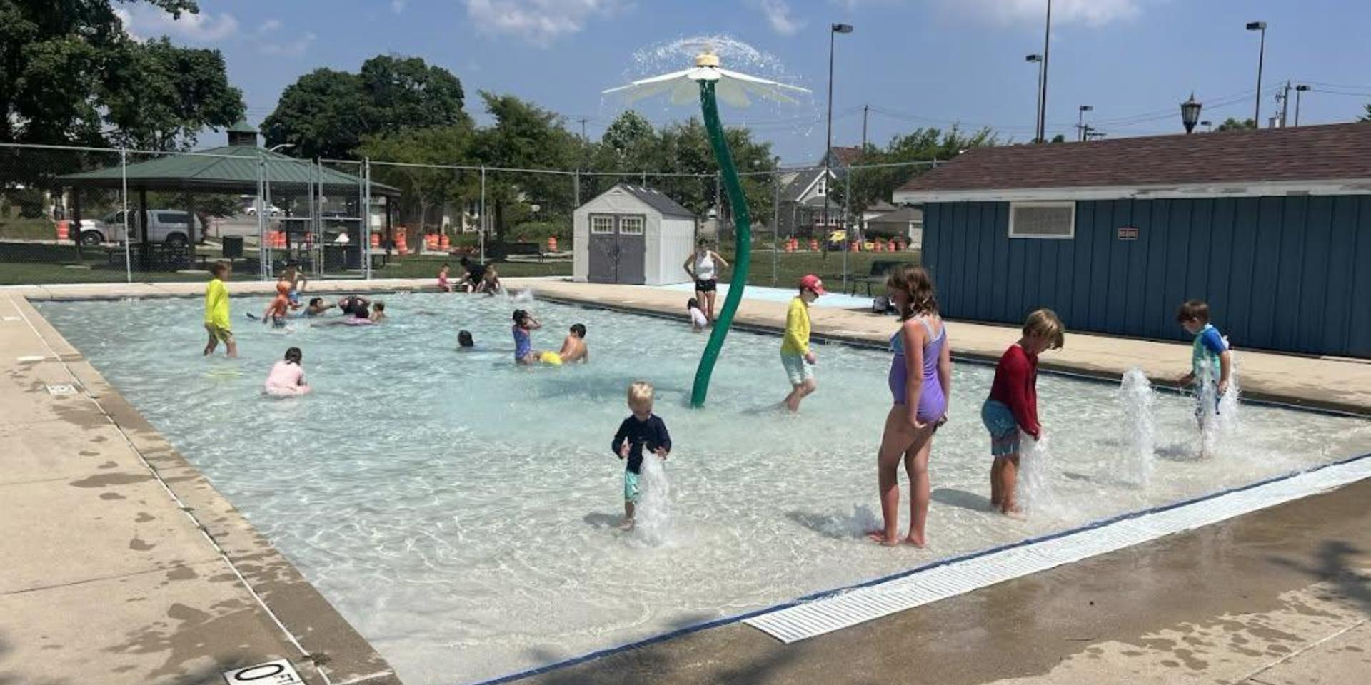 Children playing in a splash pad area at a pool on a sunny day.
