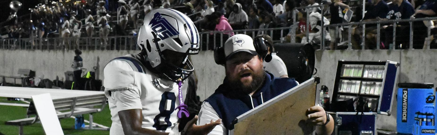Coach and player examining a playbook during a game on the sidelines.