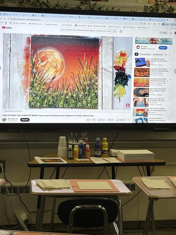Art tutorial on a screen with a painted moon over grass and various art supplies.