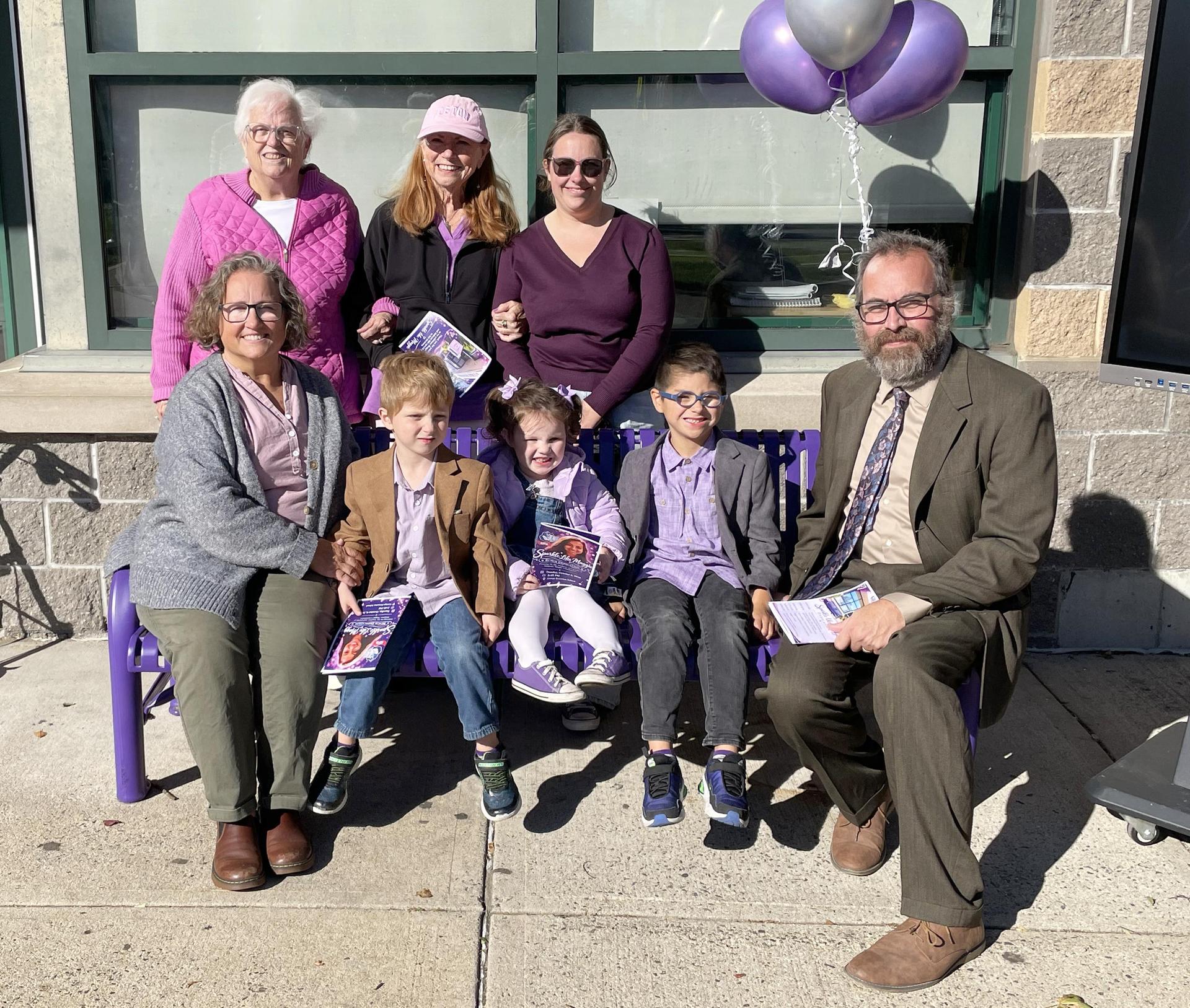 A group of adults and children sit on a bench, celebrating a special occasion.