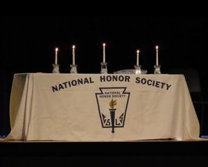 table draped in white tablecloth with National Honor Society logo. 5 lit candles on table